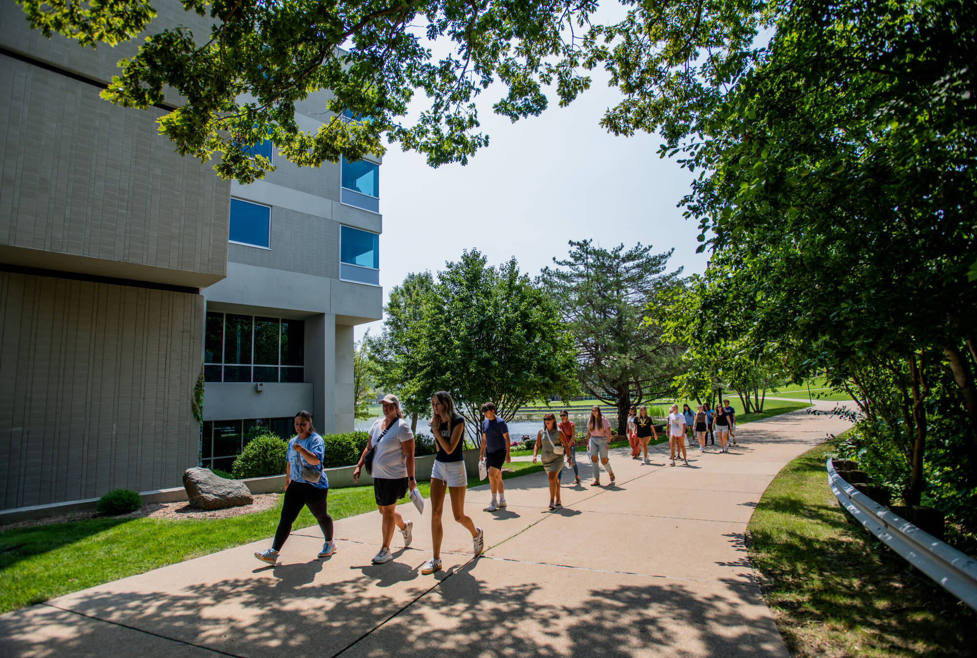 A student leads prospective students on a tour of campus on a sunny summer day.